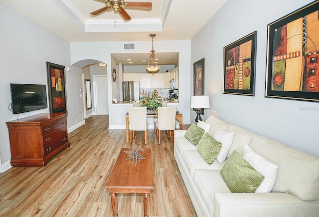 living room with ceiling fan, a tray ceiling, and light hardwood / wood-style floors