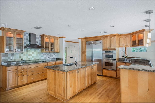 kitchen featuring appliances with stainless steel finishes, wall chimney exhaust hood, sink, and light hardwood / wood-style flooring