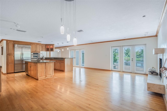 kitchen with an island with sink, hanging light fixtures, a textured ceiling, appliances with stainless steel finishes, and light wood-type flooring