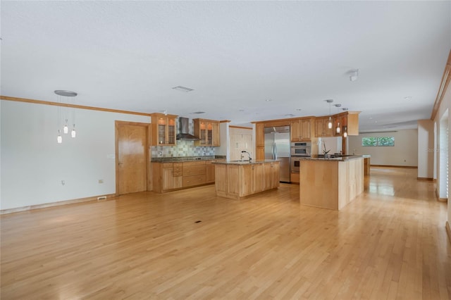 kitchen with decorative light fixtures, appliances with stainless steel finishes, wall chimney range hood, and a center island with sink