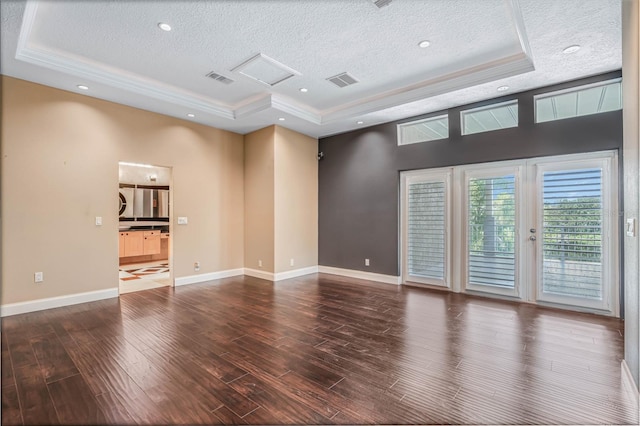 empty room with a textured ceiling, a tray ceiling, and dark hardwood / wood-style flooring