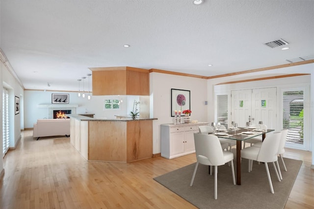 dining room with a textured ceiling, crown molding, and light hardwood / wood-style floors