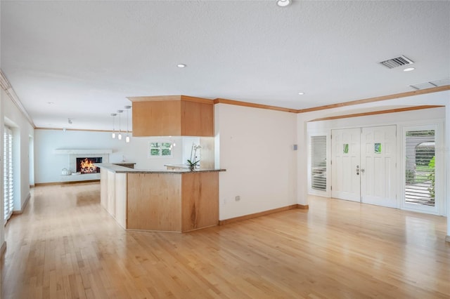 kitchen featuring light wood-type flooring, a textured ceiling, decorative light fixtures, ornamental molding, and light brown cabinetry