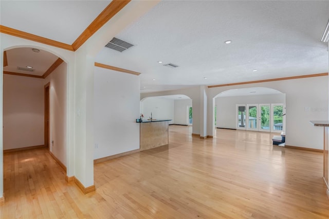 unfurnished living room with light hardwood / wood-style flooring, a textured ceiling, and ornamental molding