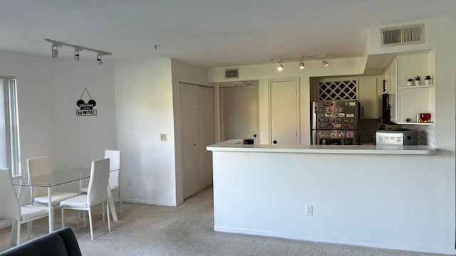 kitchen featuring light carpet, rail lighting, kitchen peninsula, and stainless steel fridge