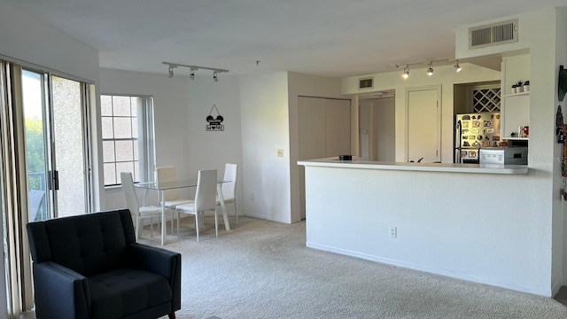 interior space featuring light carpet, kitchen peninsula, stainless steel refrigerator, and rail lighting