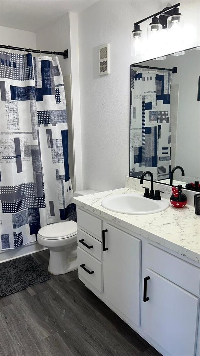 bathroom featuring a shower with shower curtain, toilet, vanity, wood finished floors, and a textured wall