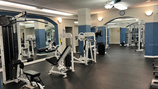 exercise room featuring decorative columns, ceiling fan, and a textured ceiling