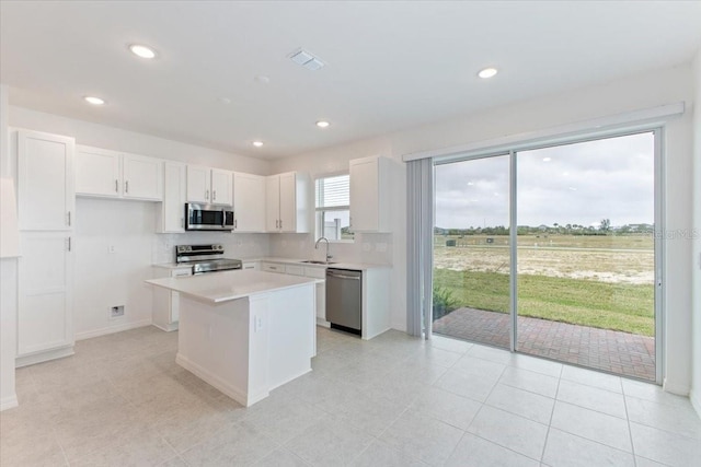 kitchen with appliances with stainless steel finishes, tasteful backsplash, sink, a center island, and white cabinetry