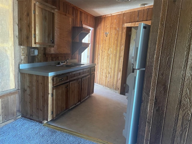 kitchen featuring light carpet, a textured ceiling, wooden walls, sink, and white fridge