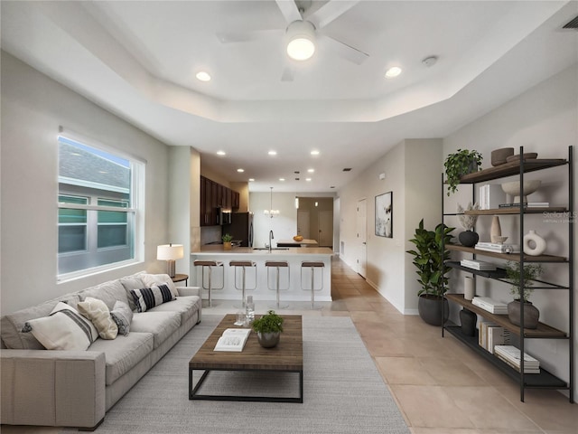 tiled living room with a tray ceiling, ceiling fan, and sink