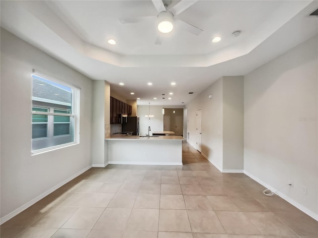 kitchen with baseboards, a tray ceiling, a peninsula, light countertops, and fridge