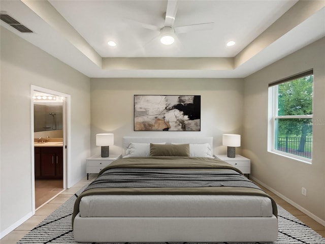 bedroom featuring a raised ceiling, ceiling fan, light wood-type flooring, and ensuite bathroom