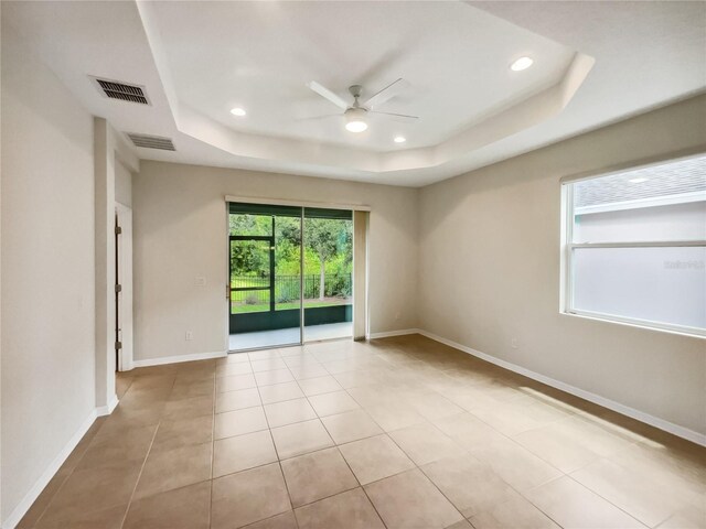 tiled empty room with a raised ceiling and ceiling fan