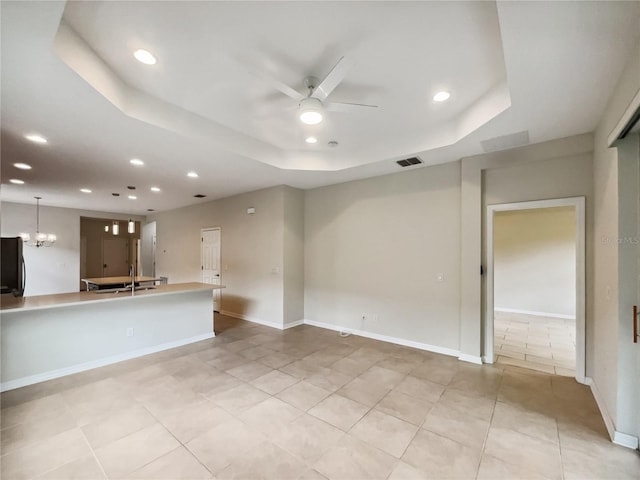 unfurnished living room featuring visible vents, baseboards, recessed lighting, ceiling fan with notable chandelier, and a tray ceiling
