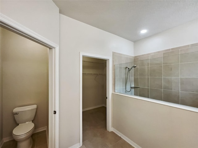 full bathroom featuring a spacious closet, tile patterned flooring, baseboards, walk in shower, and toilet