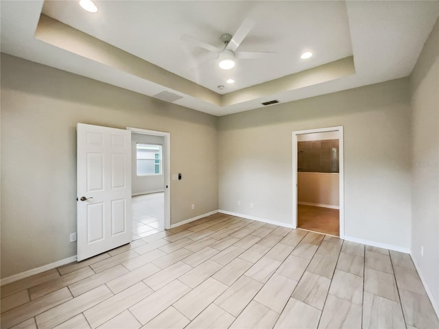 unfurnished room with a ceiling fan, a tray ceiling, baseboards, and visible vents