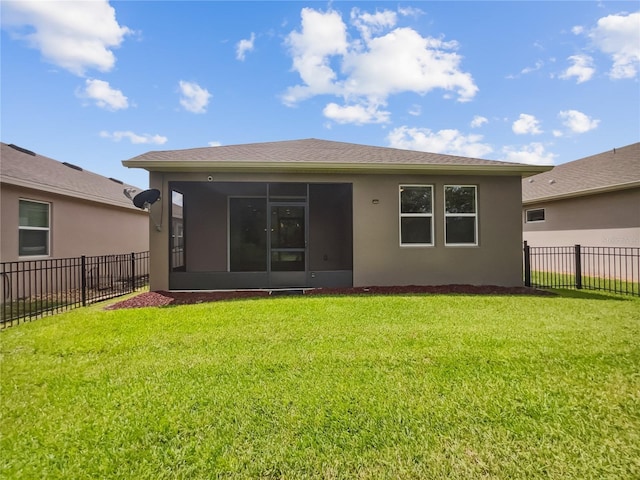 back of property with a sunroom, stucco siding, and a lawn