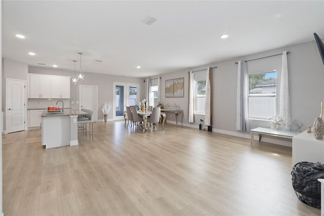 interior space featuring white cabinets, light hardwood / wood-style flooring, light stone counters, an island with sink, and pendant lighting