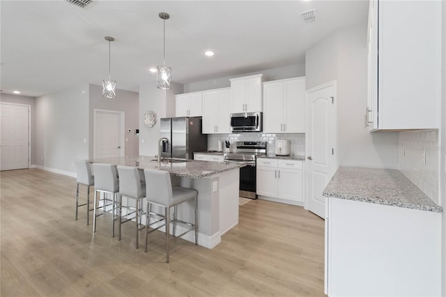 kitchen featuring a center island with sink, light stone countertops, appliances with stainless steel finishes, and white cabinets