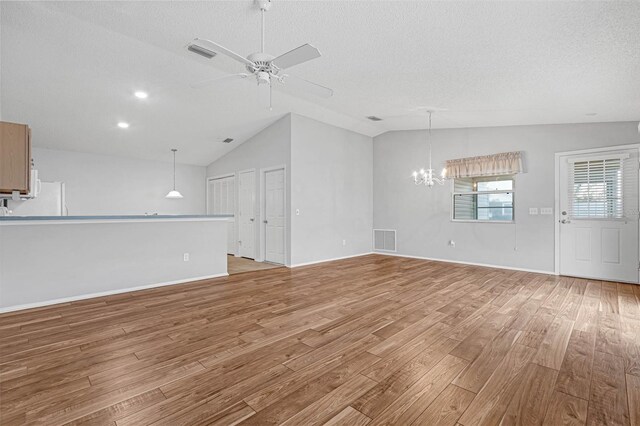 unfurnished living room featuring vaulted ceiling, ceiling fan with notable chandelier, and light hardwood / wood-style floors