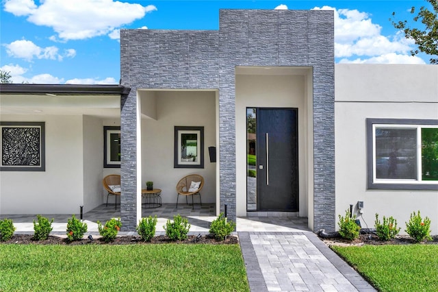 view of exterior entry featuring a lawn and a patio area