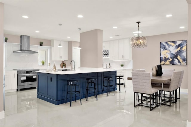 kitchen with a center island with sink, pendant lighting, stainless steel electric range oven, white cabinetry, and wall chimney range hood