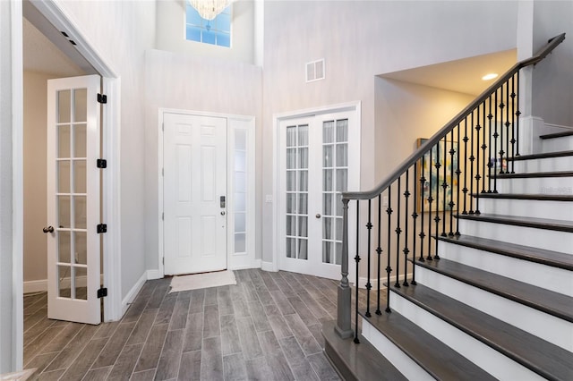 entrance foyer with an inviting chandelier, a towering ceiling, and french doors