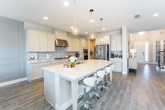 kitchen featuring a breakfast bar, white cabinets, hanging light fixtures, an island with sink, and appliances with stainless steel finishes