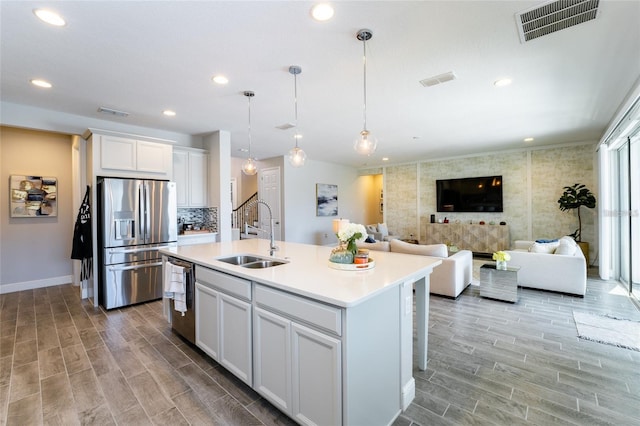 kitchen featuring sink, hanging light fixtures, stainless steel appliances, a center island with sink, and white cabinets