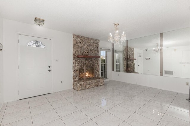 interior space with an inviting chandelier, a textured ceiling, and a stone fireplace