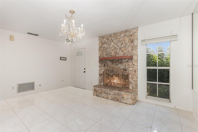 unfurnished living room featuring a textured ceiling, an inviting chandelier, a stone fireplace, and light tile patterned floors