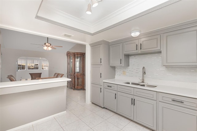 kitchen featuring light tile patterned floors, sink, a raised ceiling, ceiling fan, and ornamental molding