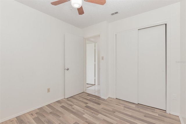 unfurnished bedroom featuring light wood-type flooring, a textured ceiling, ceiling fan, and a closet