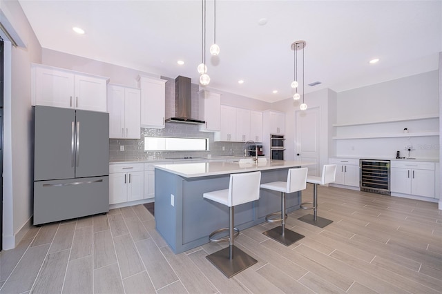 kitchen with wine cooler, wall chimney range hood, appliances with stainless steel finishes, and white cabinetry