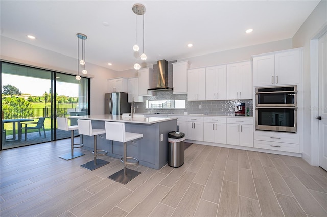 kitchen with white cabinets, stainless steel appliances, wall chimney exhaust hood, and a kitchen island with sink