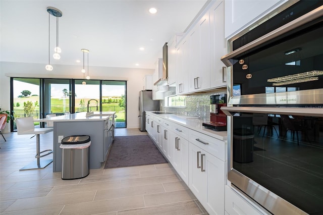 kitchen with a kitchen bar, decorative light fixtures, backsplash, an island with sink, and wall chimney range hood