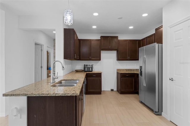 kitchen with pendant lighting, stainless steel fridge, dark brown cabinets, sink, and light hardwood / wood-style floors