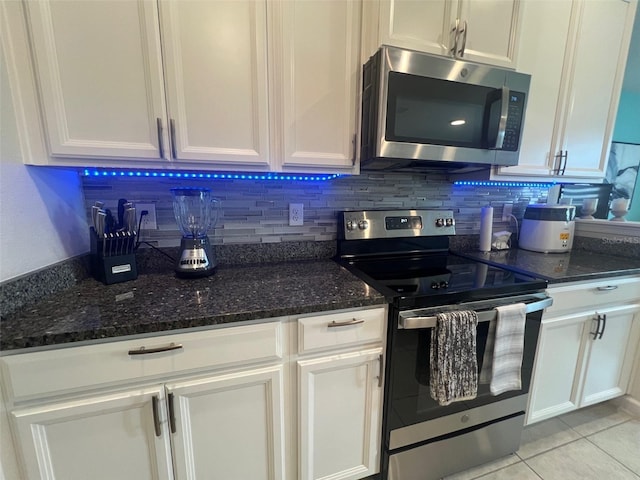 kitchen featuring stainless steel appliances, dark stone countertops, light tile patterned floors, and white cabinets