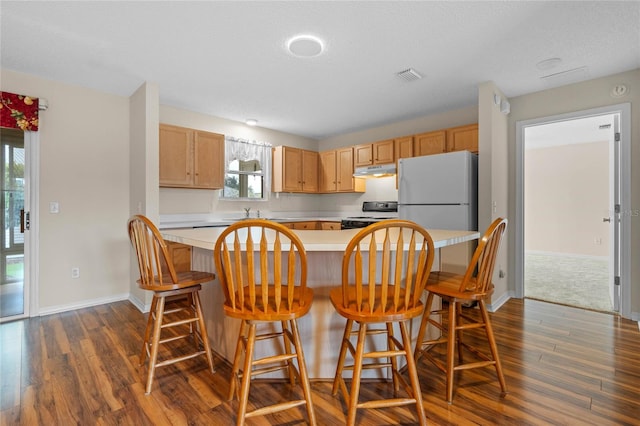 kitchen with white refrigerator, range with electric cooktop, dark wood-type flooring, a breakfast bar, and a textured ceiling