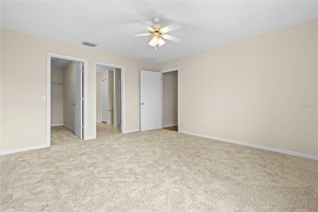 unfurnished bedroom featuring light carpet, a textured ceiling, ceiling fan, a closet, and a spacious closet