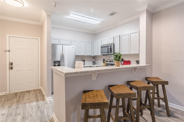 kitchen with stainless steel appliances, white cabinets, light stone counters, a kitchen bar, and crown molding