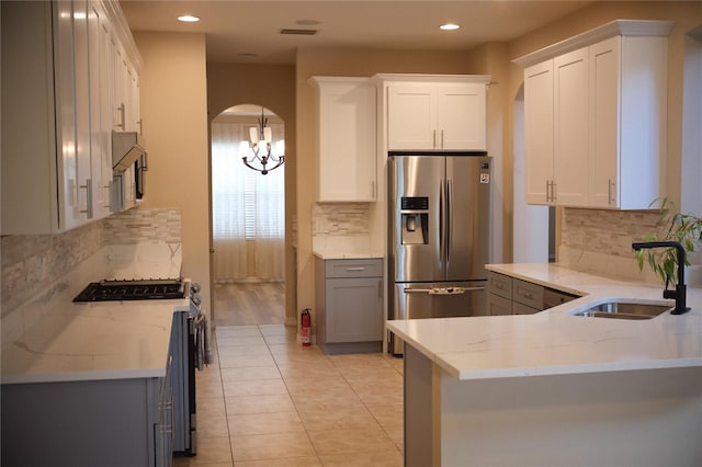 kitchen featuring hanging light fixtures, white cabinets, kitchen peninsula, light stone countertops, and stainless steel appliances