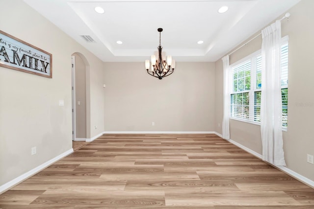 unfurnished dining area featuring a tray ceiling, a chandelier, and light wood-type flooring