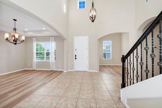 tiled foyer entrance featuring a raised ceiling, a high ceiling, and a notable chandelier