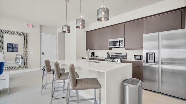 kitchen featuring light tile patterned floors, pendant lighting, stainless steel appliances, a kitchen island with sink, and sink