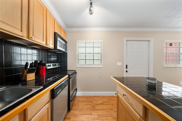 kitchen featuring ornamental molding, tile countertops, light hardwood / wood-style flooring, decorative backsplash, and appliances with stainless steel finishes