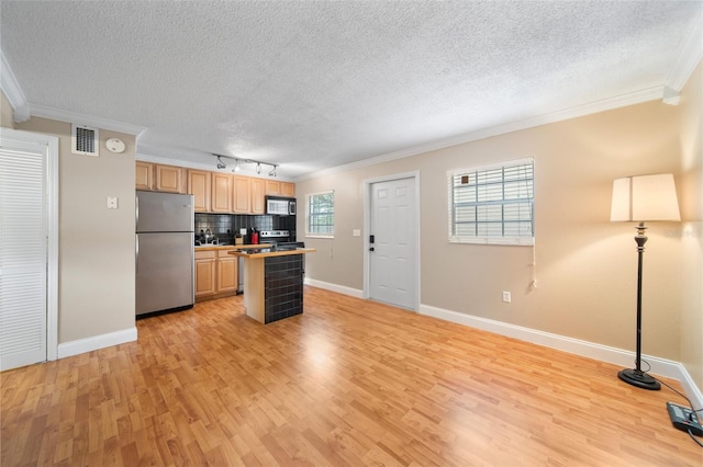 kitchen with a wealth of natural light, tasteful backsplash, appliances with stainless steel finishes, and light hardwood / wood-style floors