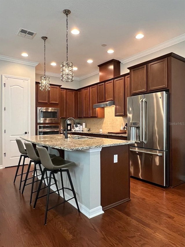 kitchen with an inviting chandelier, light stone countertops, stainless steel appliances, dark hardwood / wood-style flooring, and an island with sink