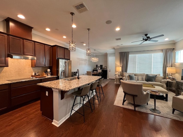 kitchen featuring ceiling fan with notable chandelier, high end refrigerator, light stone countertops, dark wood-type flooring, and a kitchen breakfast bar